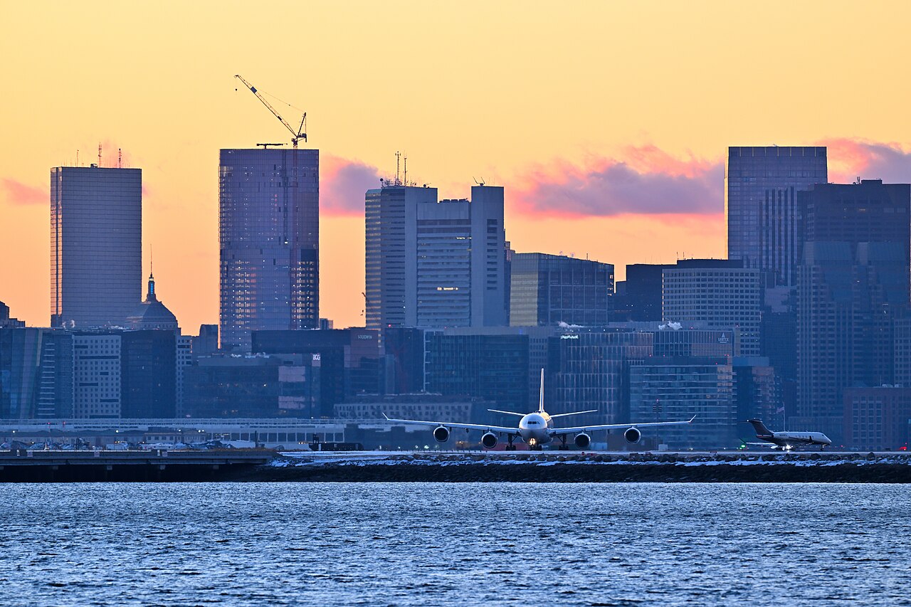 A Lufthansa airliner and a business jet at Boston Logan, with the city skyline behind them in winter evening light.