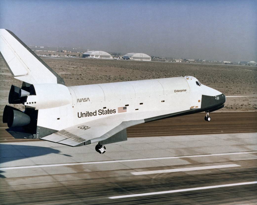 Enterprise descends toward the concrete runway with its landing gear down.