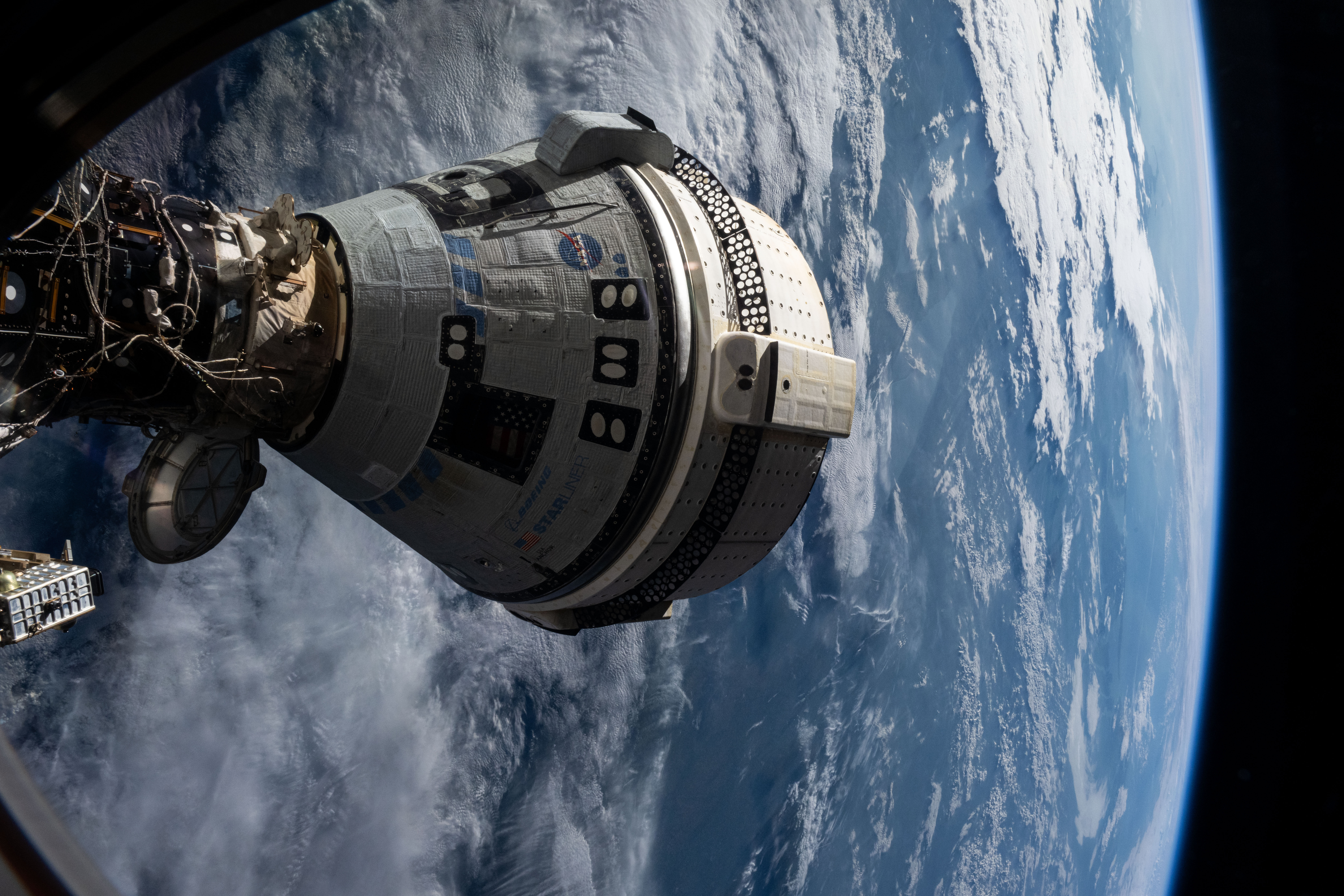 Starliner docked to the space station, with Earth behind it.