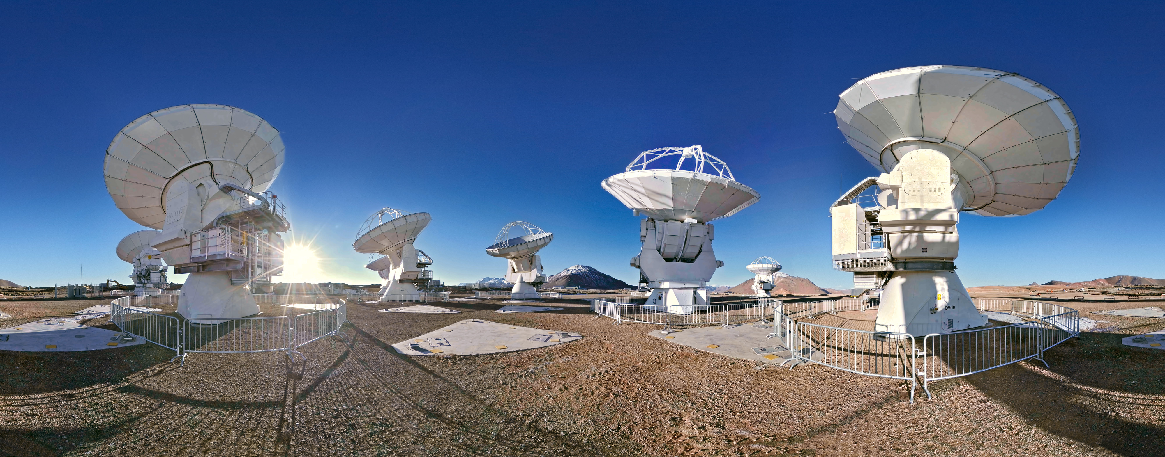 Wide daylight panorama of white ALMA antennas across Chile’s dry Chajnantor plateau.