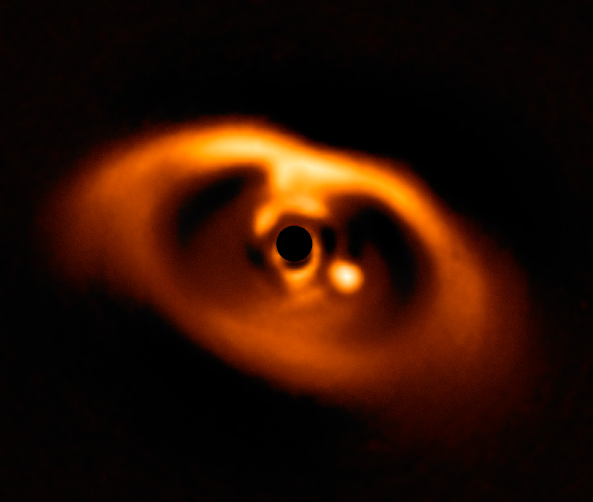 Infrared image of PDS 70 with a masked star, surrounding disk and bright planet to its right.