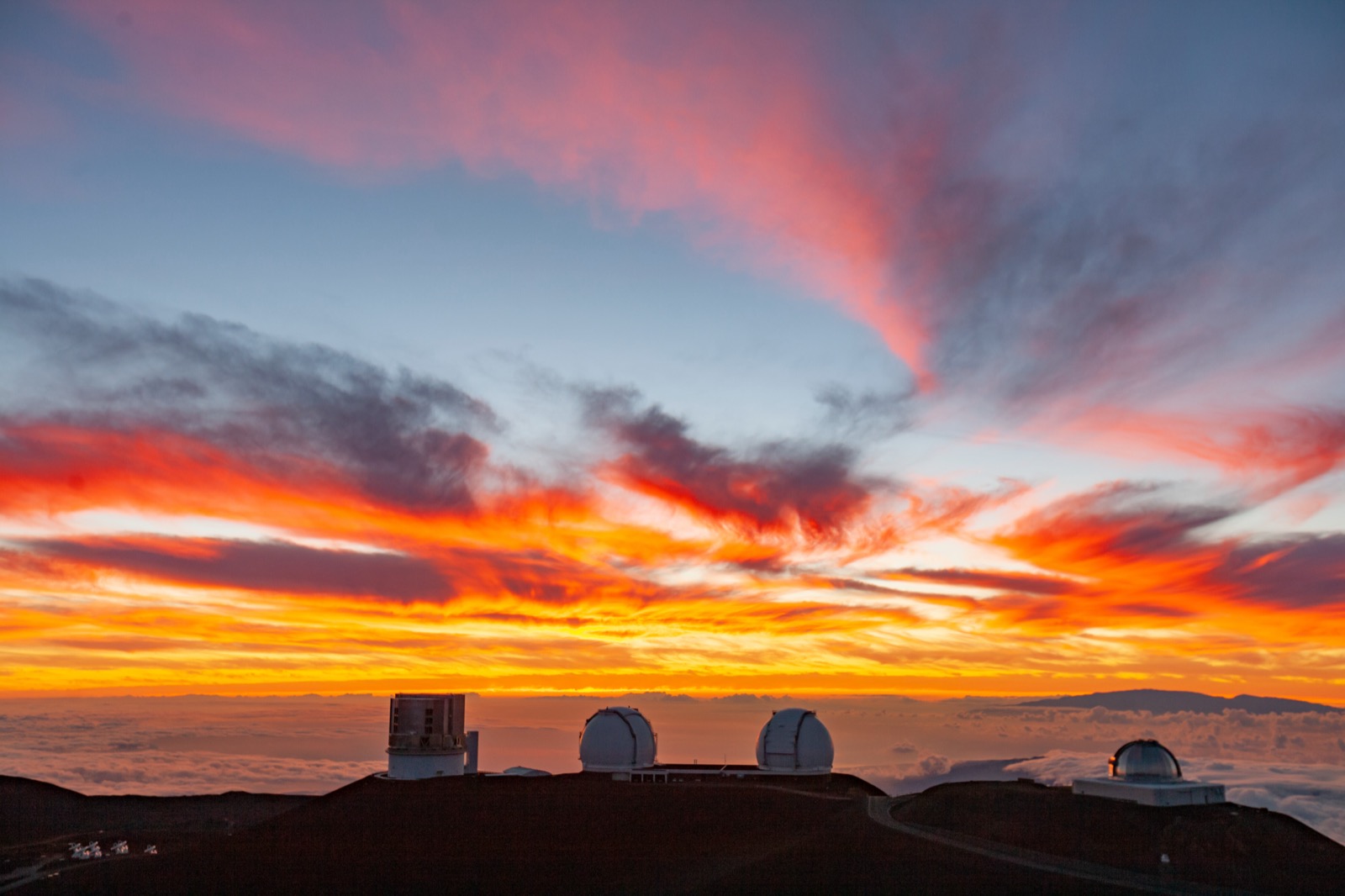 Keck’s twin telescope domes and neighboring observatories beneath a vivid Maunakea sunset.